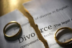 Paper with the word Divorce that is ripped in half with two wedding rings sitting on either side.