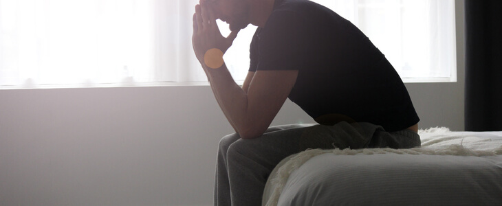 visibly stressed man, sitting on his bed