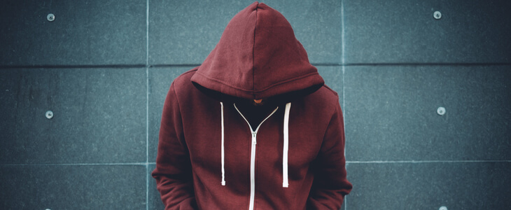 Young man wearing a red hooded sweatshirt leaning against a stone wall